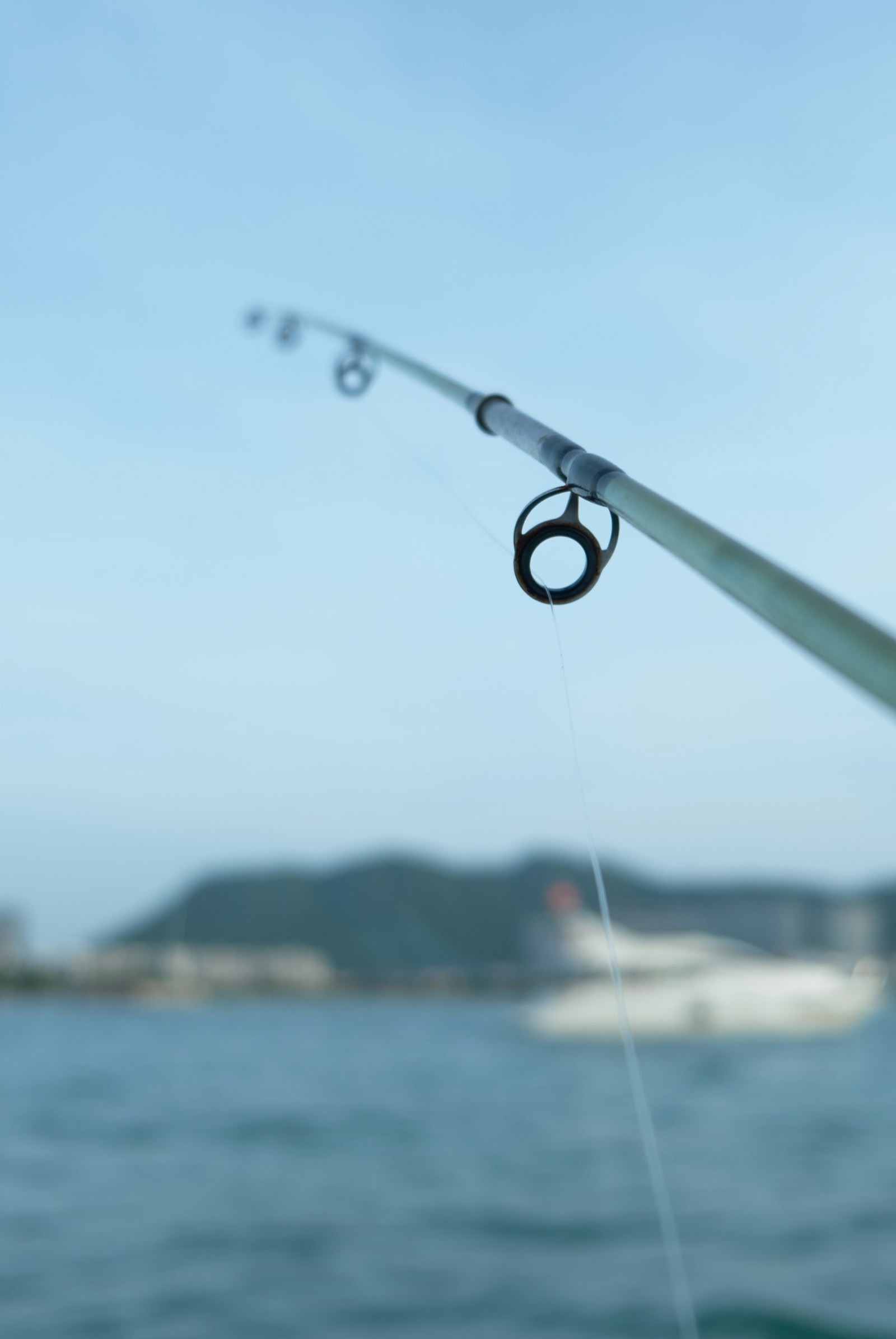 A rod tip bent over calm grey water
